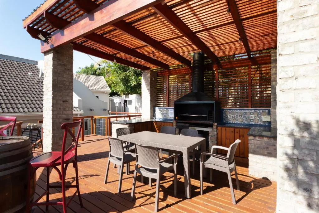 Covered outdoor deck with dining table, braai grill, and wooden pergola