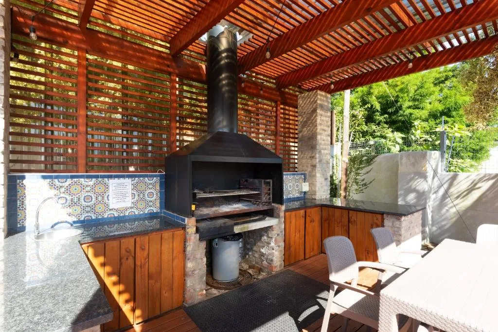 Covered outdoor patio with black braai, wooden counter, and lounge seating