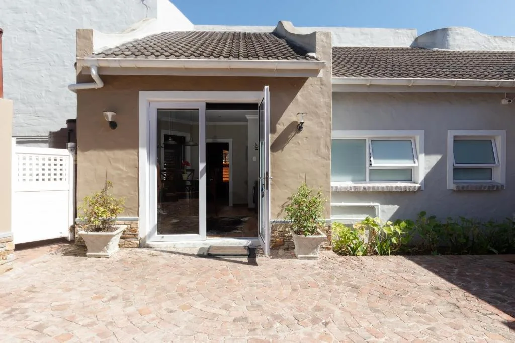 Modern home entrance with beige facade, glass doors, and brick paving
