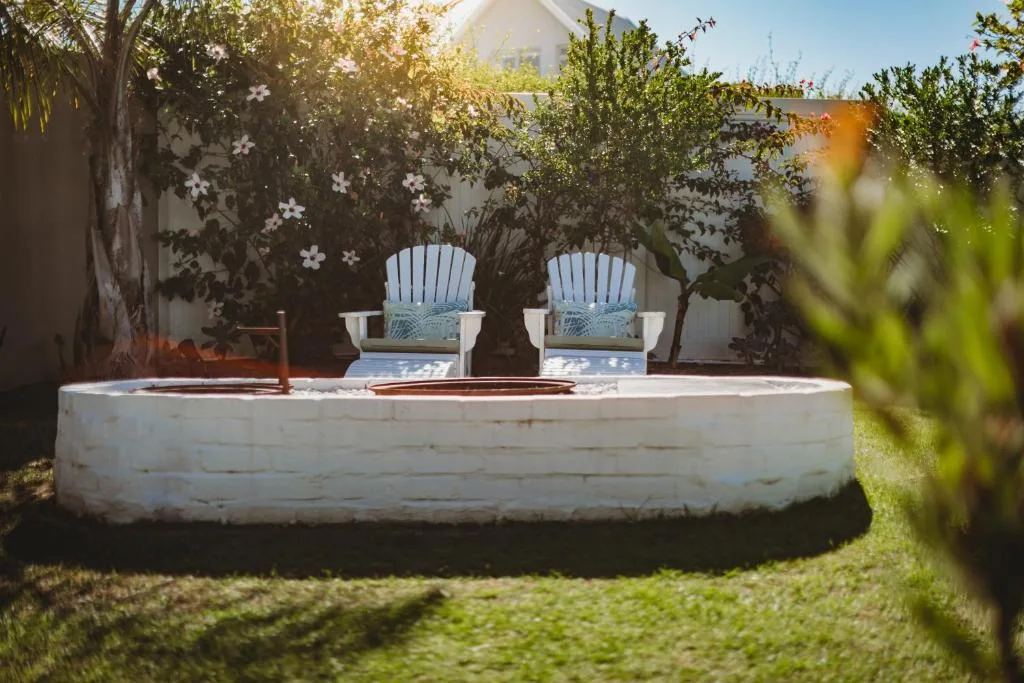 Circular fire pit seating area with blue Adirondack chairs in lush garden