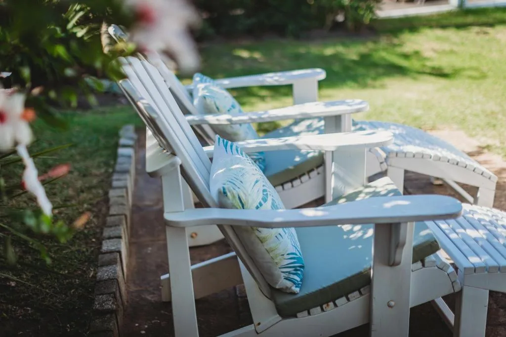 White Adirondack chairs with blue cushions arranged on a garden lawn