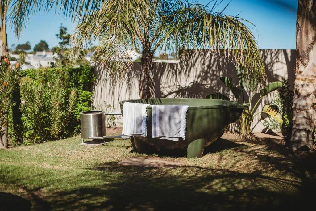 Rustic outdoor bathtub with towels drying under a weeping willow tree