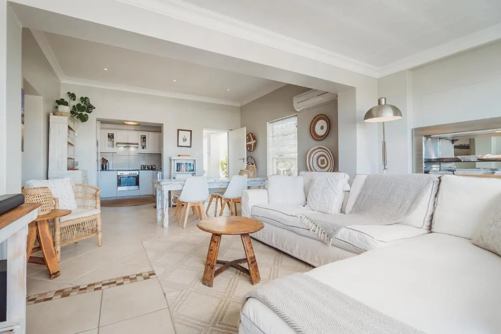 Bright open-plan lounge with white sofas, wooden accents, and kitchen visible