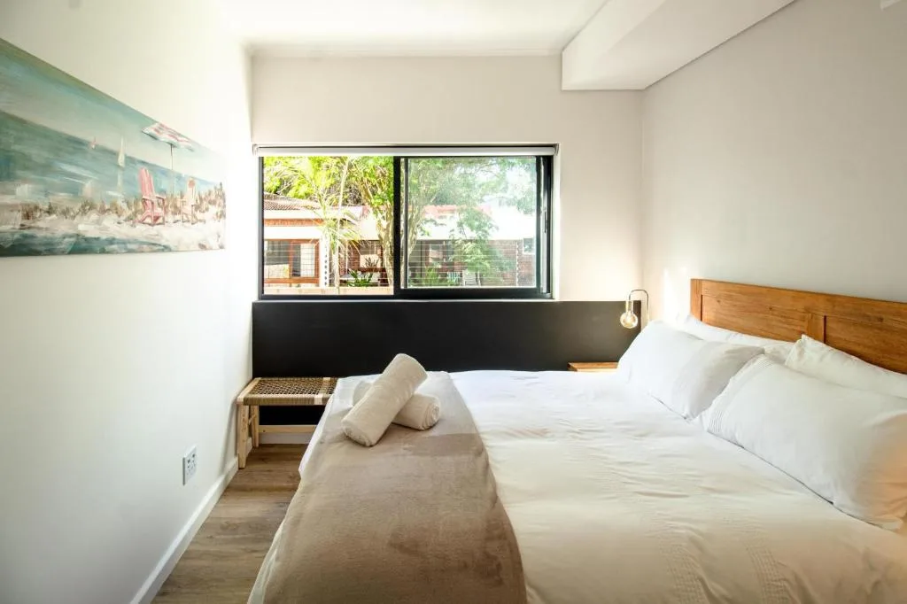 Bright bedroom with wooden bed frame and white linens, large windows