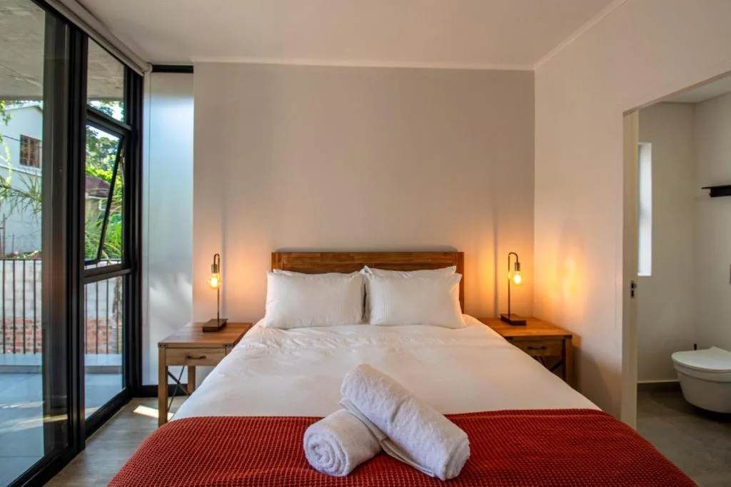 Bright bedroom with wooden bed, white linens, red runner, and deck access