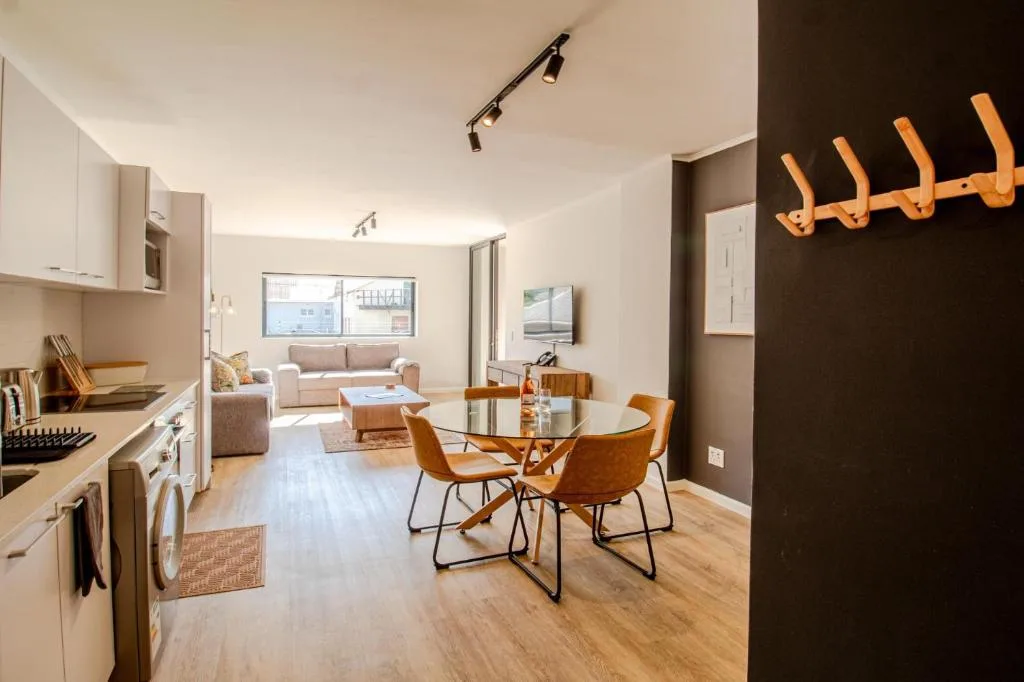 Modern dining area with round glass table and wooden chairs, open-plan kitchen and lounge beyond