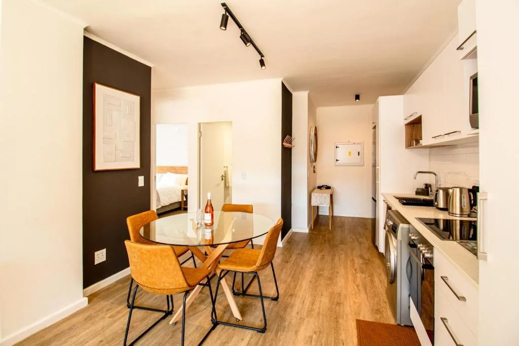 Open-plan dining area with round table and orange chairs, kitchen visible