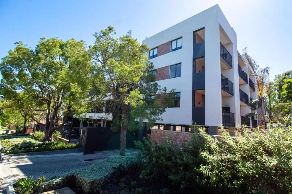 Modern white apartment building with brick accents and landscaped garden surroundings