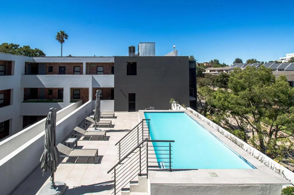 Turquoise swimming pool on modern rooftop deck with loungers and garden views