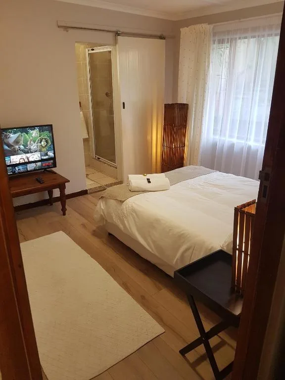 Bright bedroom with white bed, TV, and ensuite bathroom entrance visible