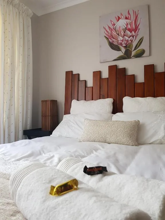 Bedroom with wooden headboard, white linens, and protea artwork on wall