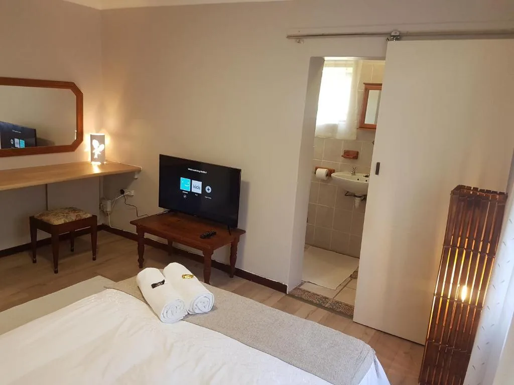 Modern bedroom with bed, TV, desk, and ensuite bathroom entrance visible