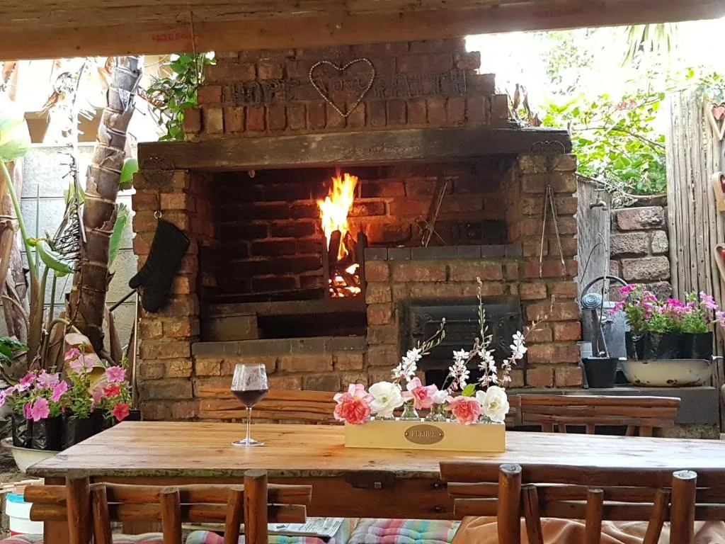 Outdoor braai area with active fireplace, wooden table, and pink flowers