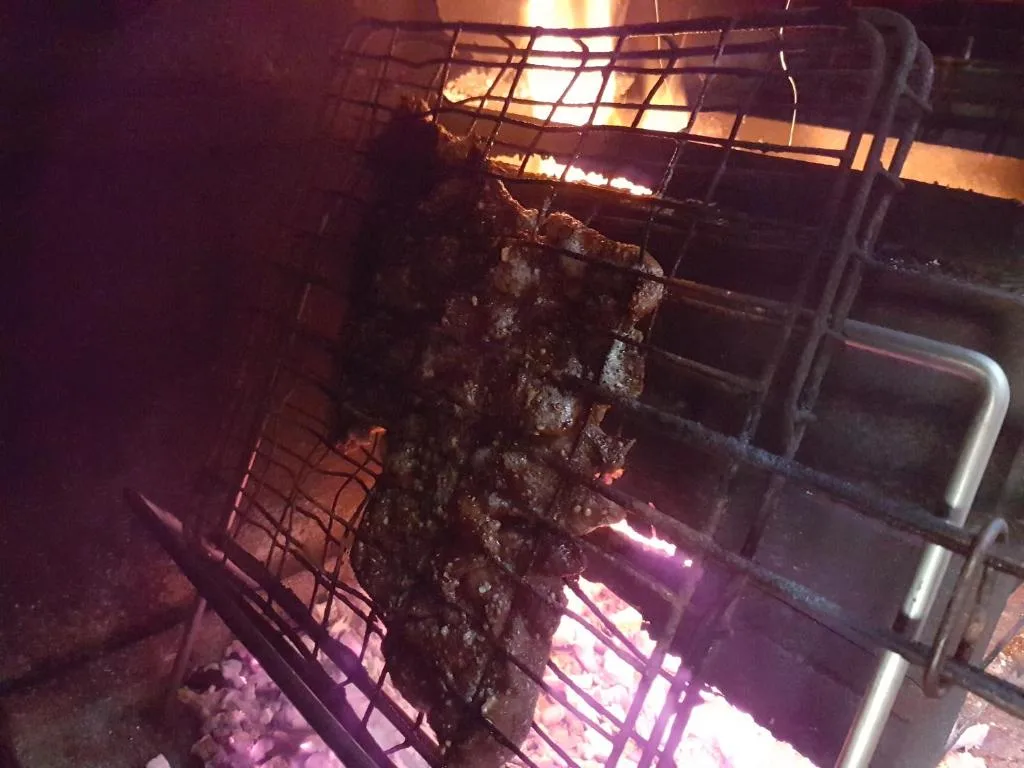 Close-up of braai grill with meat cooking over open flames at night