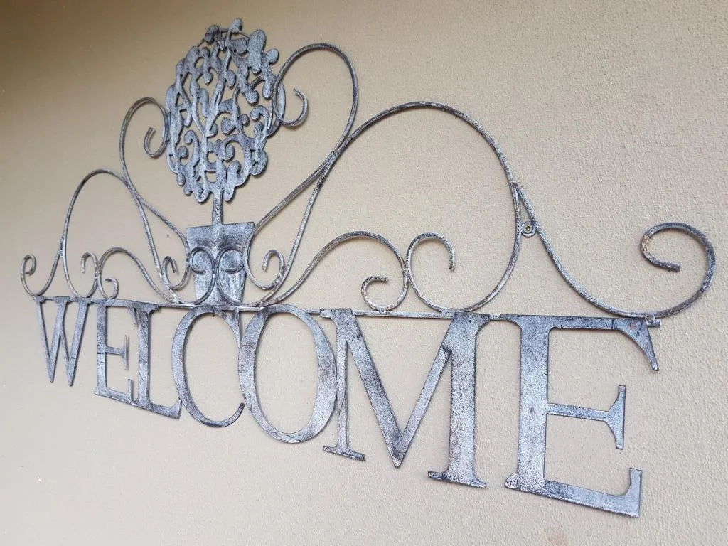 Decorative wrought-iron welcome sign mounted on beige wall