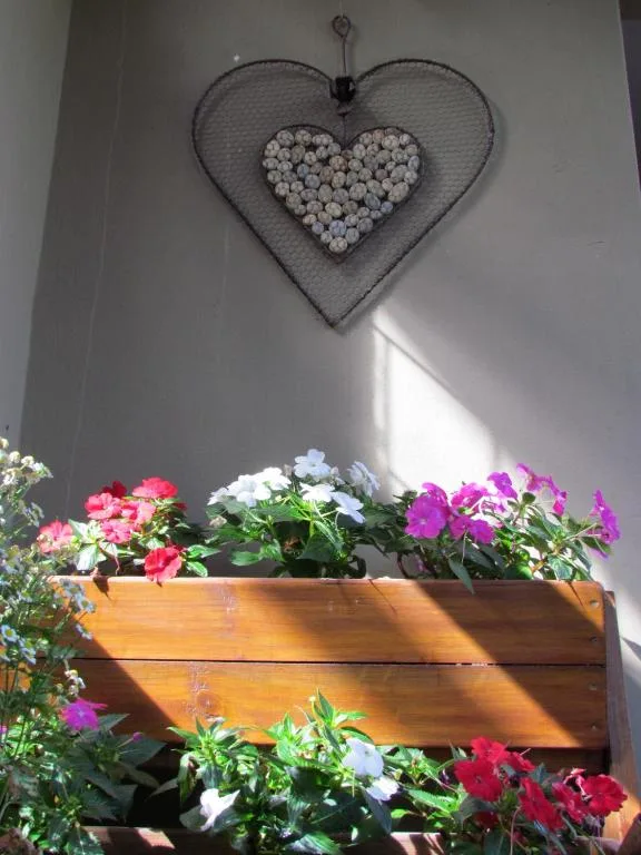 Decorative heart wall hanging above wooden planter with colorful flowers