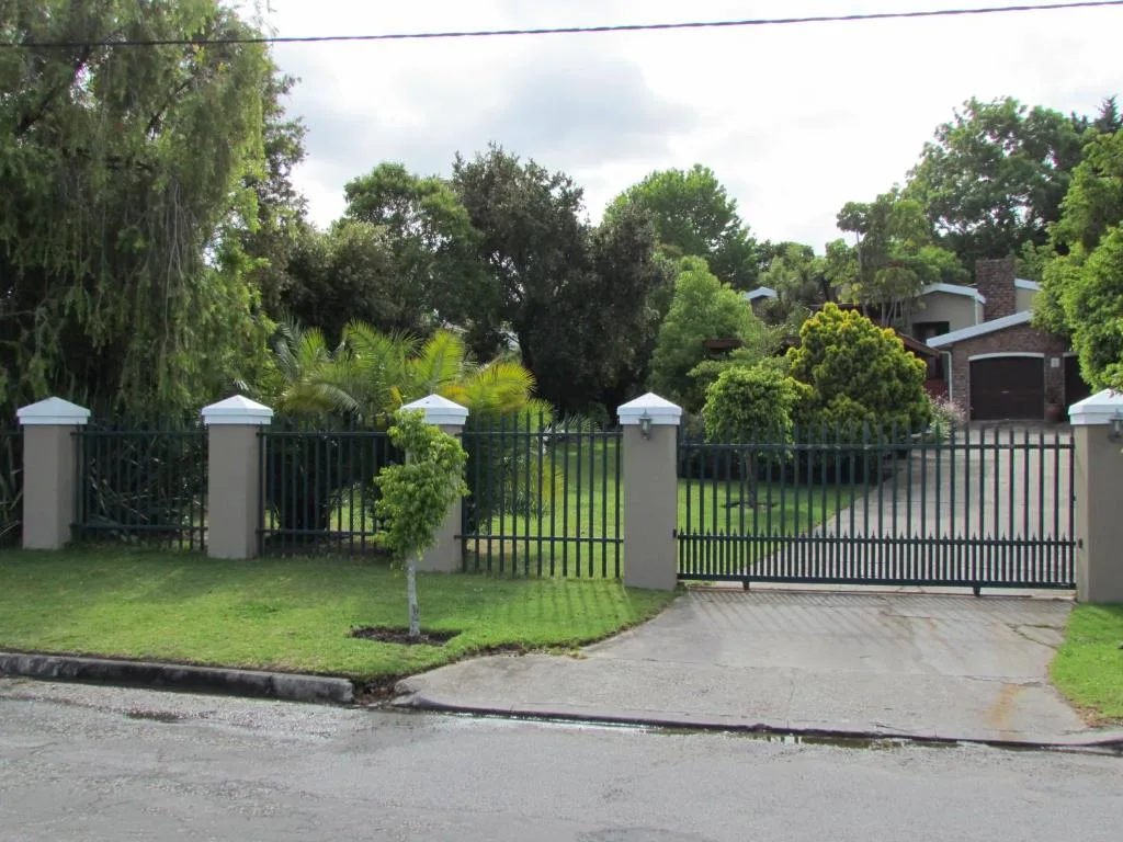 Gated driveway entrance with manicured lawn and mature trees beyond