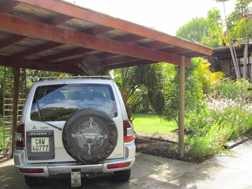 White Mitsubishi vehicle parked under wooden carport with lush garden surroundings