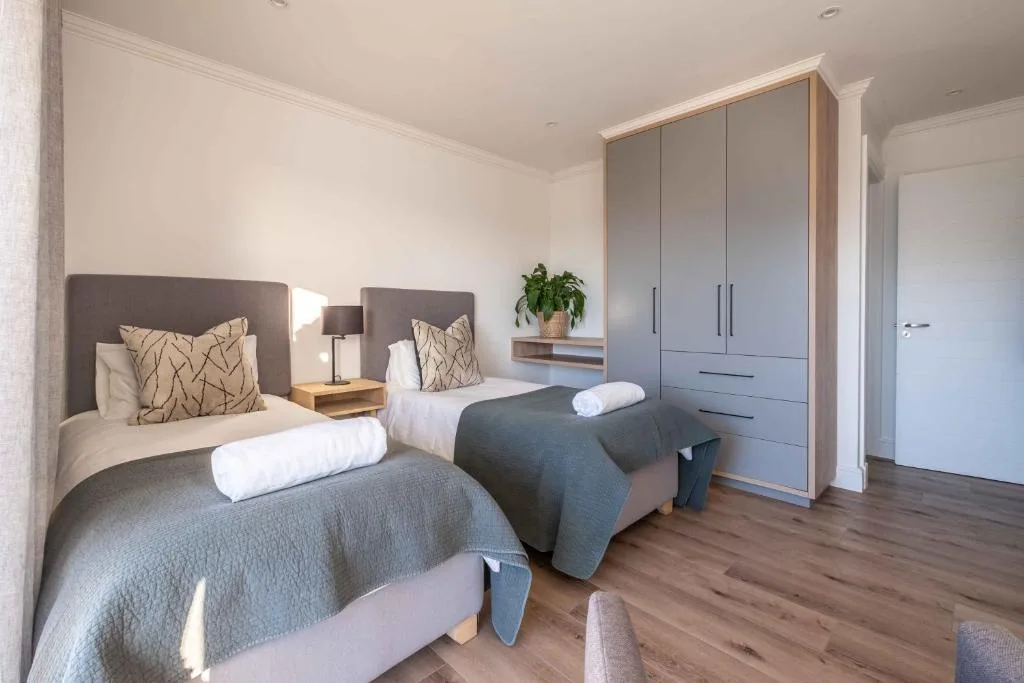 Modern twin bedroom with gray headboards, potted plant, and built-in wardrobe