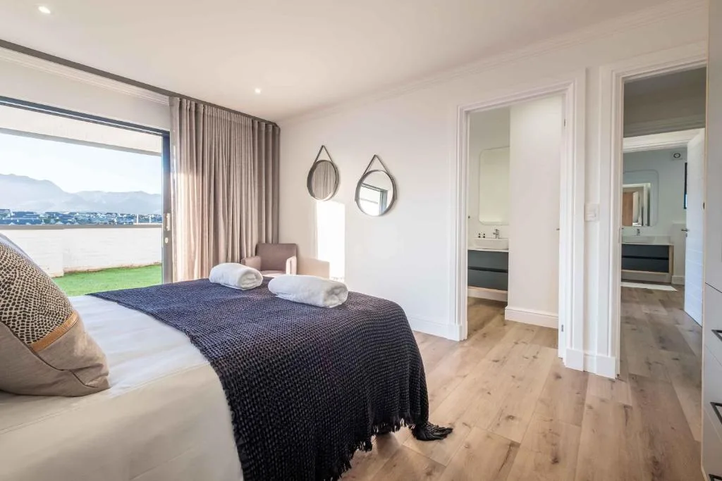 Modern bedroom with coastal view, bed with dark throw, decorative mirrors