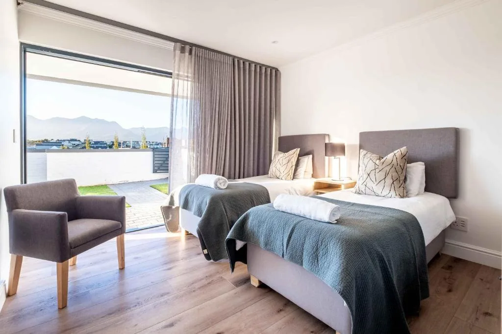 Modern bedroom with twin beds, lounge chair, mountain views through glass doors