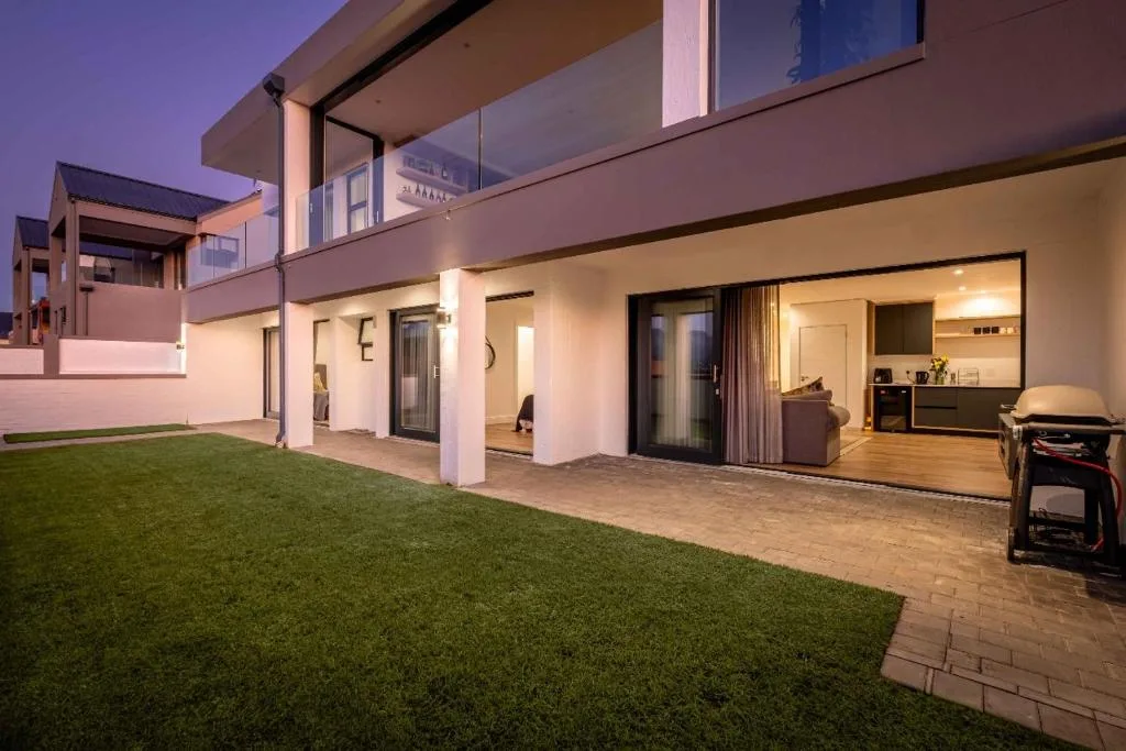 Modern home exterior with manicured lawn and paved patio area at dusk