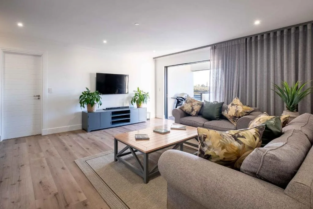 Modern living room with gray sofas, wall-mounted TV, and lagoon views through glass doors