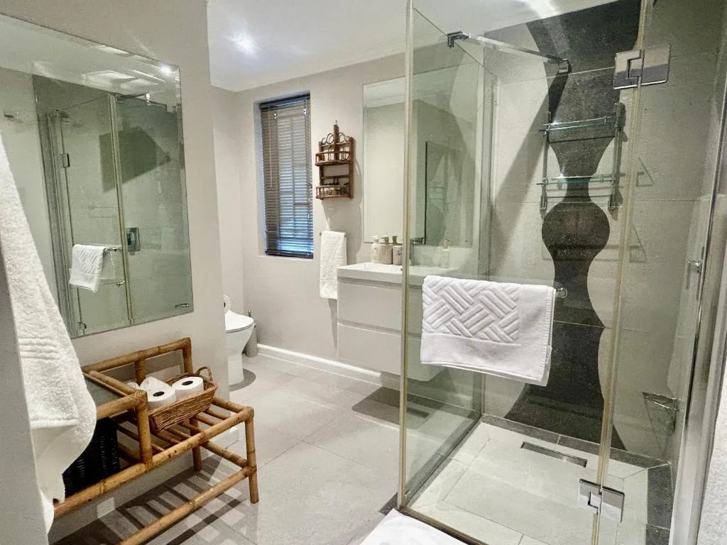 Modern bathroom with large glass shower enclosure and wooden storage bench
