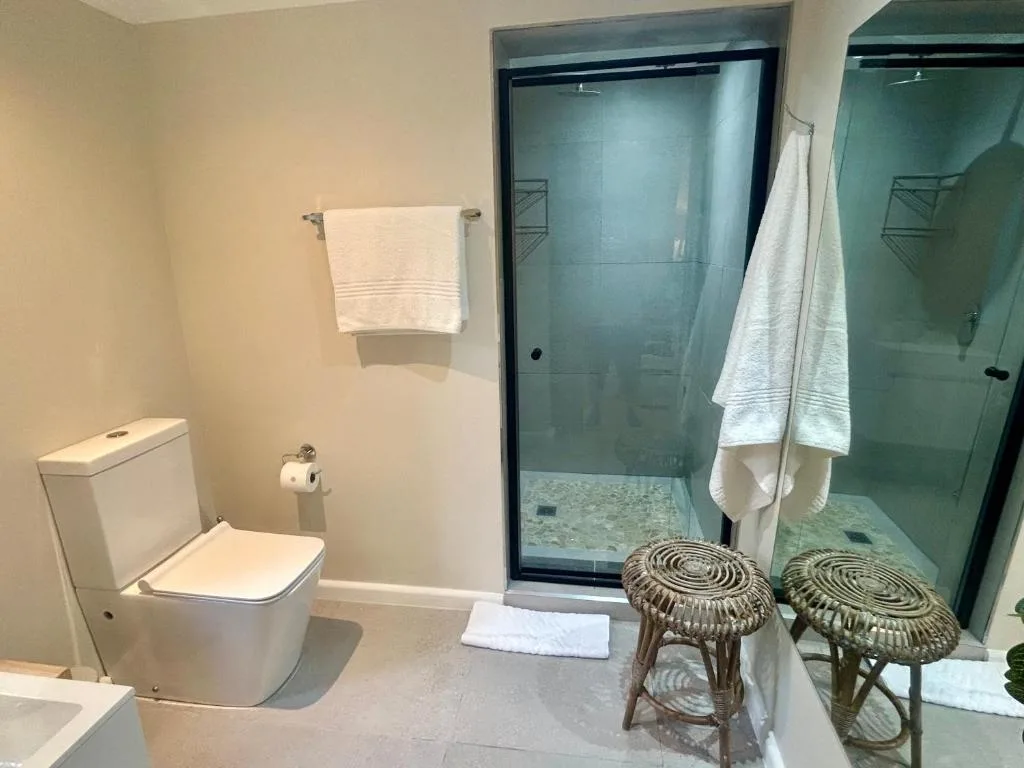 Modern bathroom with toilet, glass shower enclosure, and woven stools