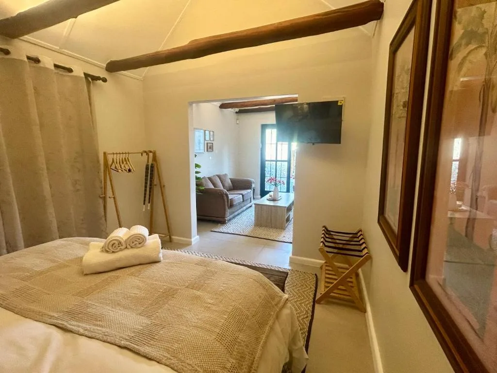 Spacious bedroom with queen bed, wooden beams, and lounge view beyond