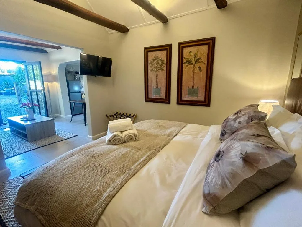 Spacious bedroom with queen bed, tropical artwork, exposed beams, and open-plan living area visible beyond.