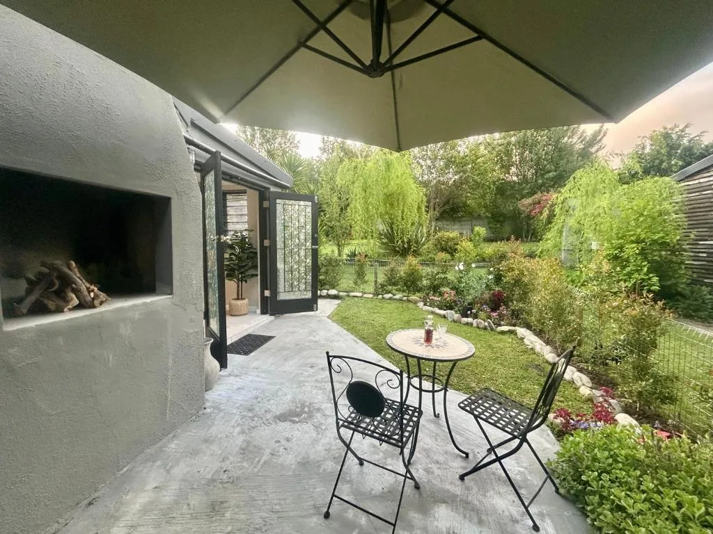 Shaded patio with table, chairs, and fireplace overlooking lush garden