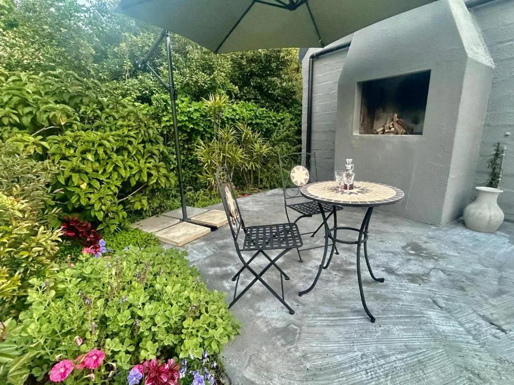 Outdoor patio with table, chairs, umbrella, fireplace, and lush garden