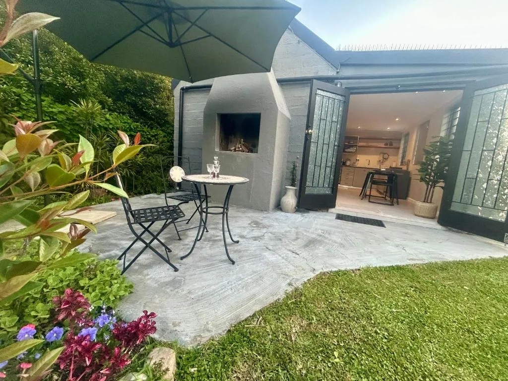 Outdoor patio with dining table, umbrella, fireplace, and lush gardens
