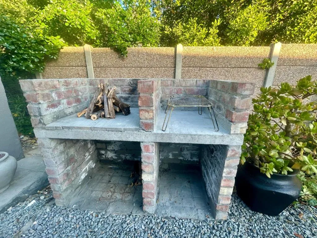 Built-in brick braai with grill grates and firewood in garden area
