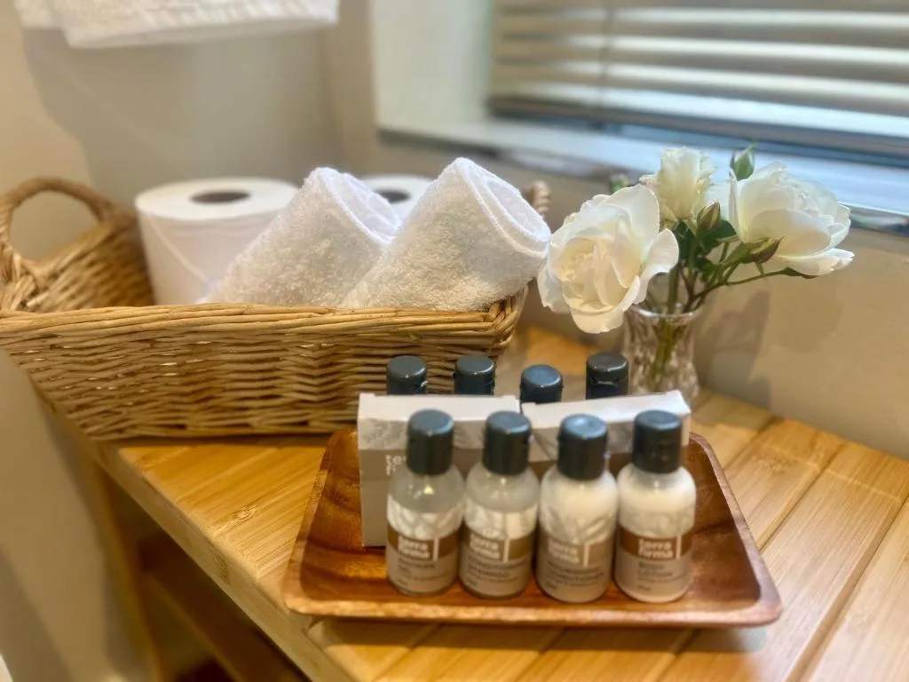 Bathroom amenities displayed with rolled towels, toiletries, and fresh flowers
