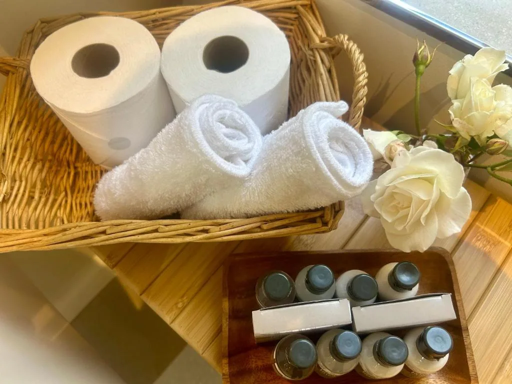 Bathroom amenities basket with rolled towels, toiletries, and fresh flowers
