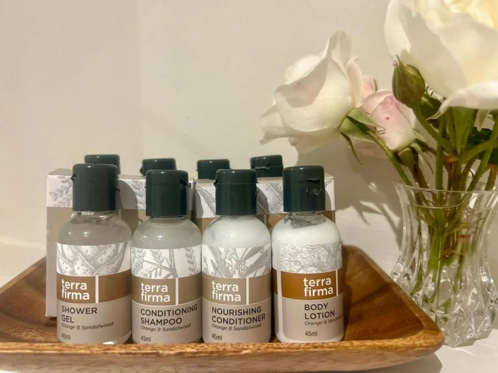 Bathroom amenities set with terra firma toiletries and fresh white roses in glass vase