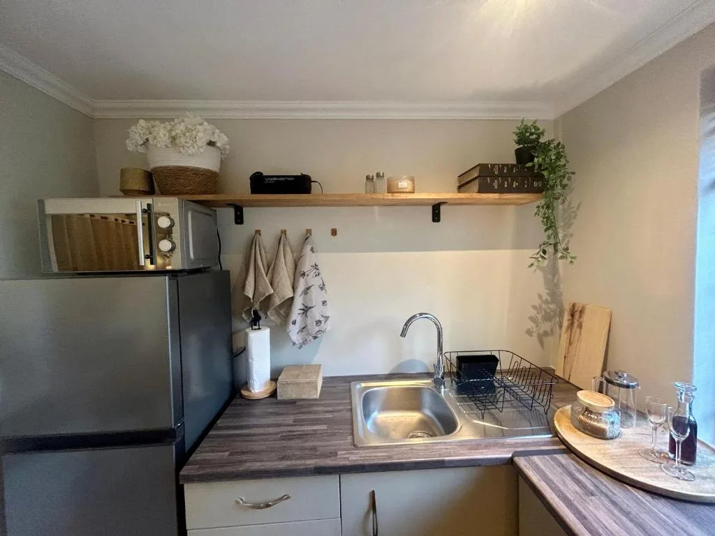Compact kitchen with stainless steel sink, microwave, and wooden shelving