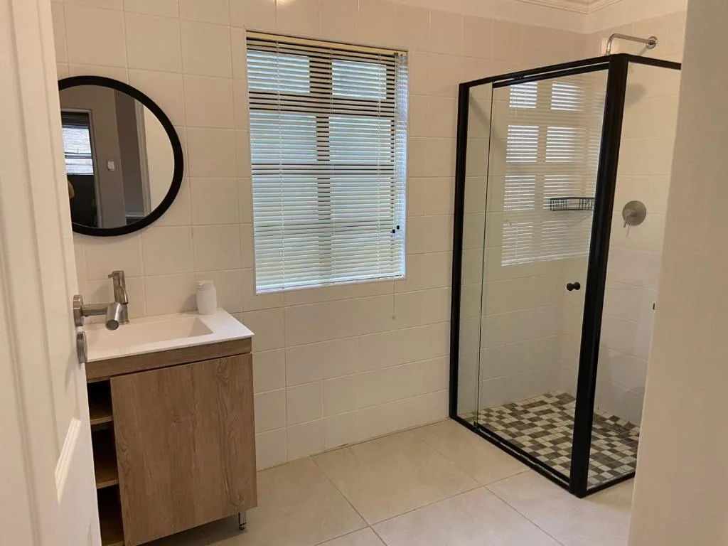 Modern bathroom with vanity sink, round mirror, and glass shower enclosure with black frame