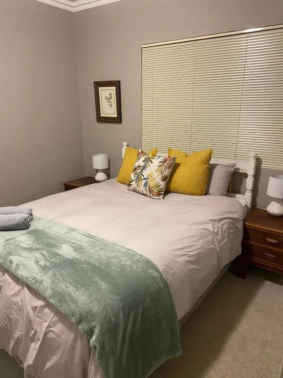 Neatly made bed with yellow and patterned pillows, wooden bedside tables