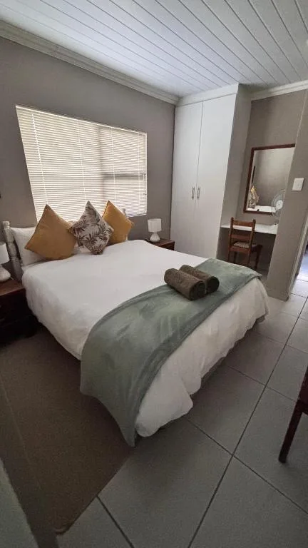 Bright bedroom with white bed, gold cushions, and en-suite bathroom visible