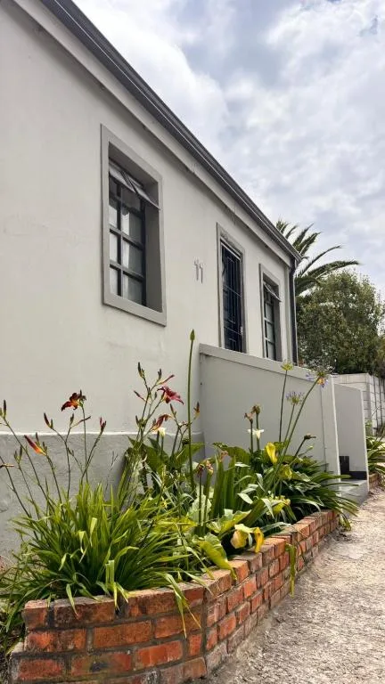 White cottage facade with black-framed windows and colorful flower garden beds