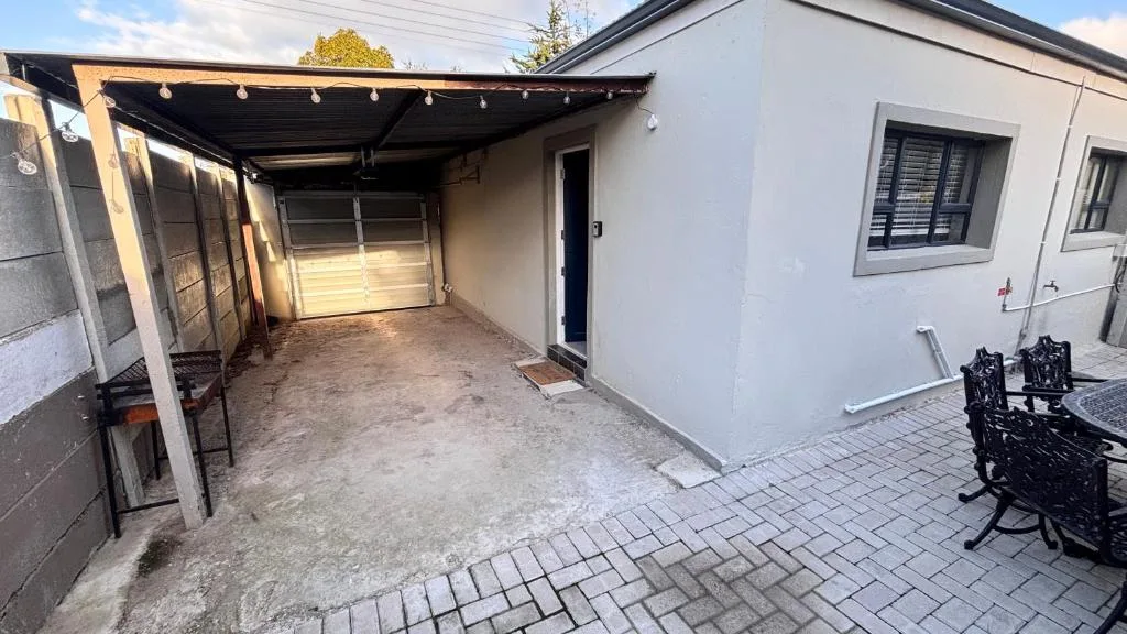 Modern white cottage with carport, paved driveway, and black chairs visible