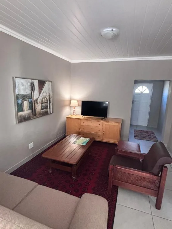Bright lounge with TV, wooden dresser, armchair, and burgundy rug