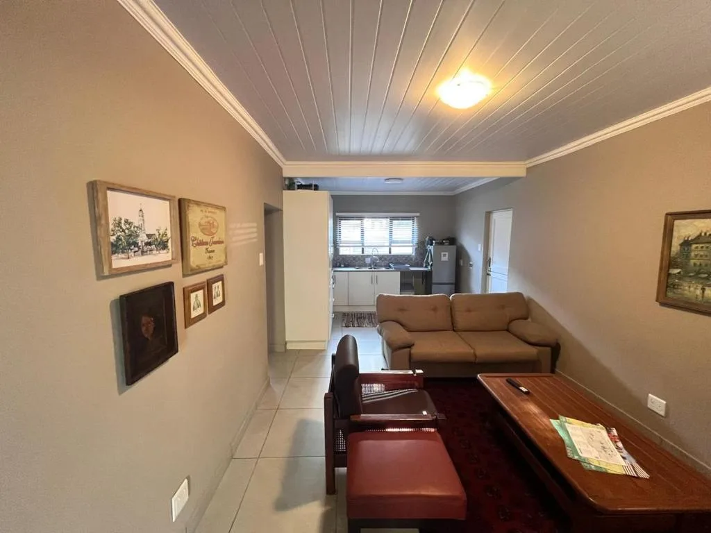 Open-plan living area with brown sofa, dining table, and kitchen visible