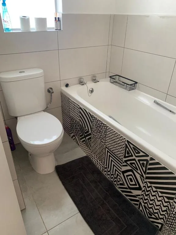 Clean bathroom with toilet, bathtub, and geometric patterned shower curtain