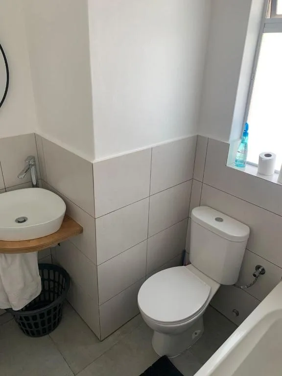 Modern bathroom with toilet, round sink, tiled walls, and bright window