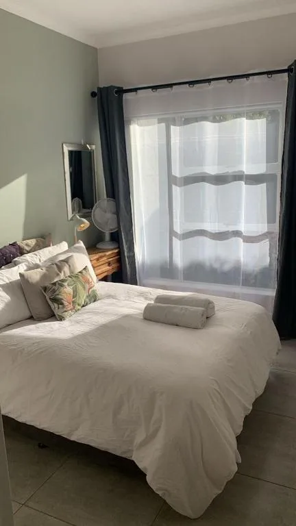 Bright bedroom with white bedding, decorative pillows, and large windows with sheer curtains