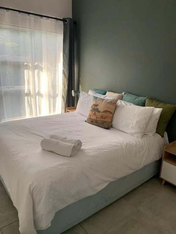 Spacious bedroom with white linens, green accent wall, and natural light